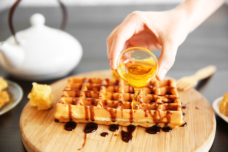 Female hand pouring honey on wafflesの写真素材