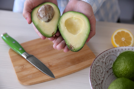 Woman holding fresh avocado in kitchenの写真素材