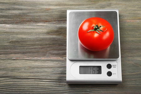 Tomato with digital kitchen scales on wooden backgroundの写真素材