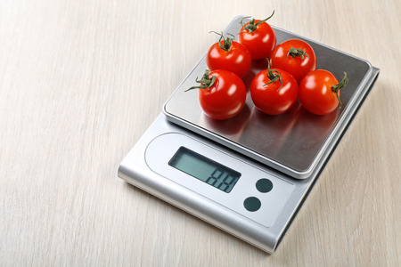 Tomatoes with digital kitchen scales on wooden backgroundの写真素材