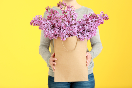 Woman holding bouquet of purple lilac flowers in paper bag on yellow backgroundの写真素材