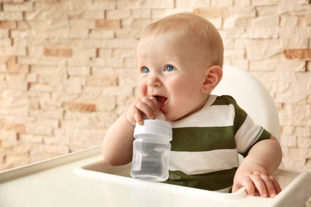 Baby drinking water in a chair on brick wall backgroundの写真素材