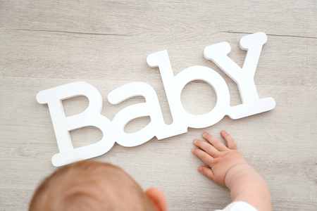 Baby boy playing with letters of the word baby on the floorの写真素材
