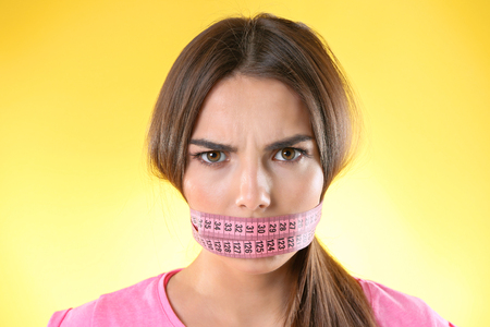 Woman with locked mouth for diet on yellow backgroundの写真素材