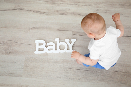 Baby boy playing with letters of the word baby on the floorの写真素材