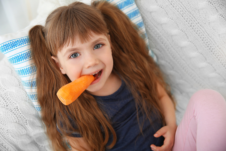 Little girl with carrot sitting on sofaの写真素材
