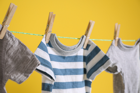 Baby clothes hanging on rope on yellow backgroundの写真素材