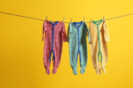 Baby clothes hanging on rope on yellow background
