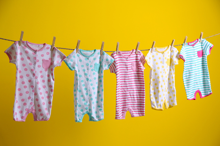 Baby clothes hanging on rope on yellow backgroundの写真素材