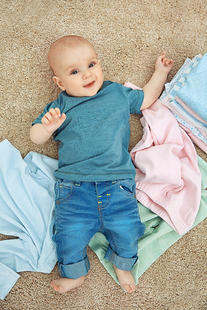 Smiling adorable baby with different clothes on the floorの写真素材