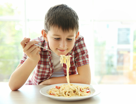 Cute boy eating spaghetti on kitchenの写真素材