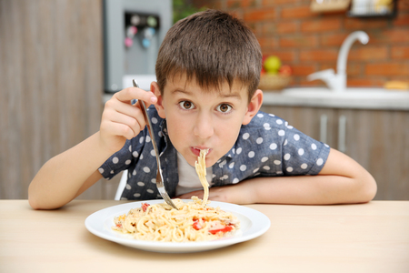 Cute boy eating spaghetti on kitchenの写真素材