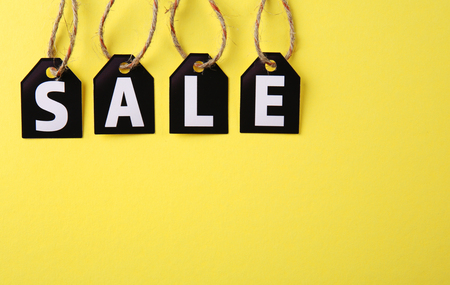 Black paper tags with strings on yellow background. Sale conceptの写真素材