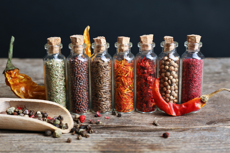 Different spices in small glass bottles on wooden tableの写真素材