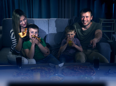 Happy lovely family watching TV with pizzaの写真素材