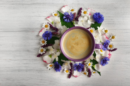 Cup of coffee with fresh flowers lying around on wooden backgroundの写真素材
