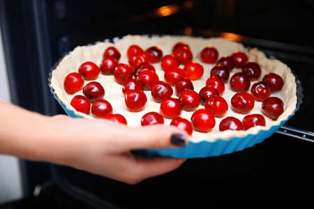 Female hand placing baking dish with cherry pie into ovenの写真素材