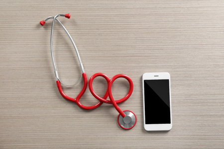 Red stethoscope with cellphone on wooden tableの写真素材