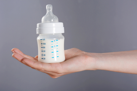 Female hand holding a baby bottle of milk on color backgroundの写真素材