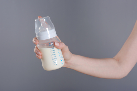 Female hand holding a baby bottle of milk on color backgroundの写真素材