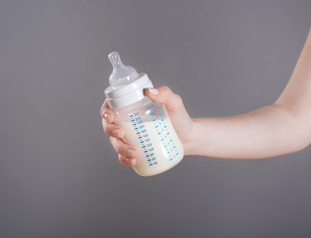 Female hand holding a baby bottle of milk on color backgroundの写真素材