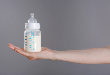 Female hand holding a baby bottle of milk on color backgroundの写真素材