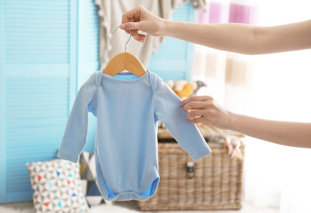 Female hand holding baby bodysuit in interior of child's roomの写真素材