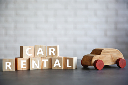 Cubes with words CAR RENTAL and wooden toy on brick wall backgroundの写真素材