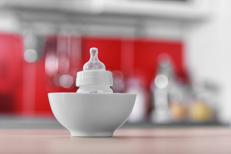 Baby bottle in bowl on kitchen tableの写真素材