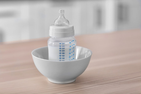 Baby bottle in bowl on kitchen tableの写真素材