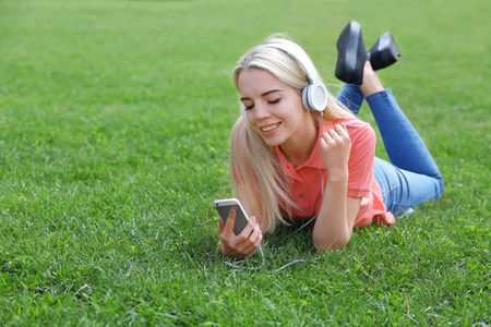 Young beautiful woman with headphones lying on the grass and listening to musicの写真素材
