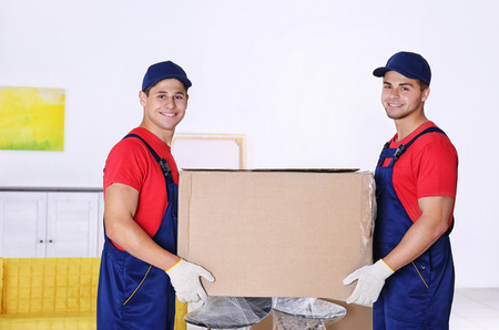 Male workers with box and furniture in new houseの写真素材