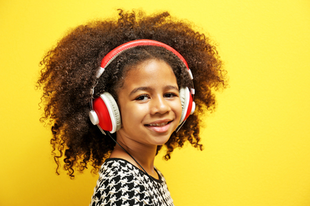 Afro-American little girl with headphones on yellow backgroundの写真素材