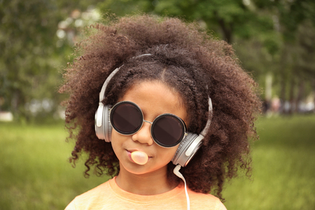 Afro-American little girl with sunglasses and headphones chewing bubblegum in parkの写真素材