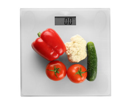 Bathroom scale with vegetables on white background
