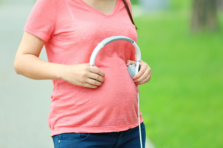 Pregnant woman with headphones on her tummy outdoorsの写真素材