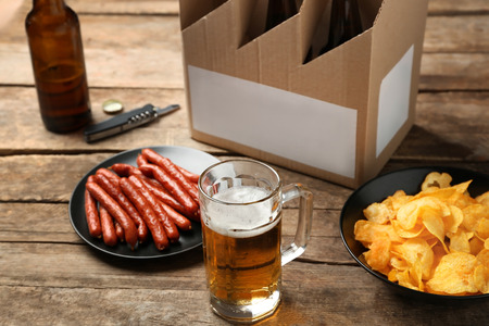 Mug of beer with snack and paper package on wooden backgroundの写真素材