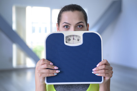 Young woman hiding behind scales on blurred background
