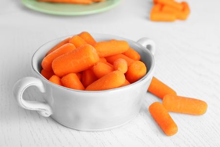 Small baby carrots in bowl on light wooden backgroundの写真素材
