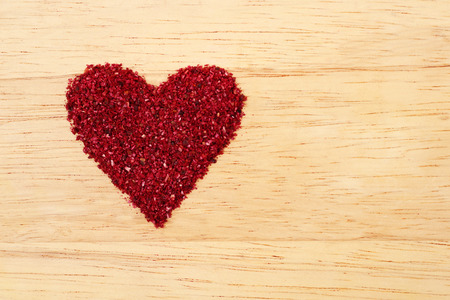 Heart shape heap of dried sumac on light wooden backgroundの写真素材
