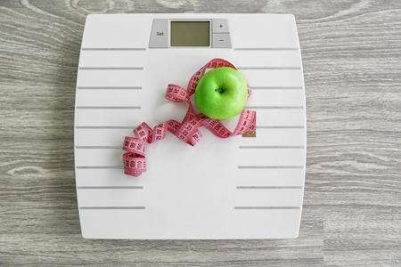 White floor scales and apple on wooden background