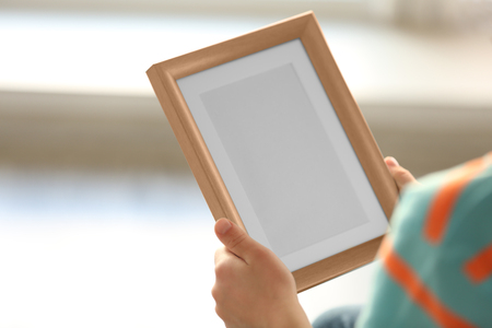 Child's hands holding photo frame on light backgroundの写真素材