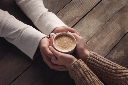Lovely couple holding cup of coffee in hands on wooden backgroundの写真素材
