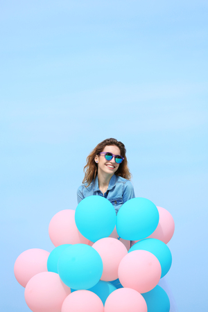 Beautiful young woman with colorful balloons against blue skyの写真素材