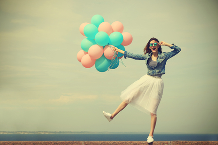 Beautiful young woman with colorful balloons on sea frontの写真素材