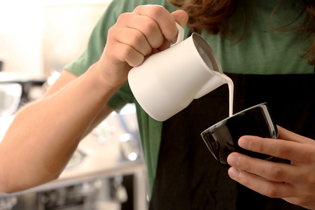 Man pouring cream in coffeeの写真素材