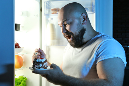 Man eating at night next to refrigeratorの写真素材