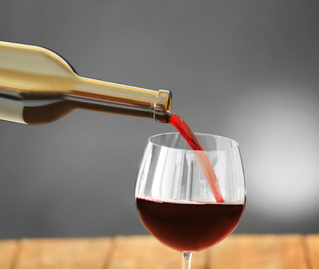 Red wine pouring in glass on grey background