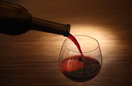 Red wine pouring in glass on wooden backgroundの写真素材