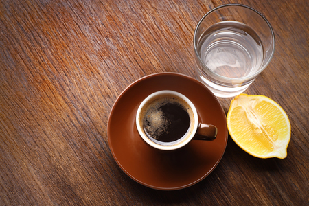 Cup of coffee with lemon and water on tableの写真素材